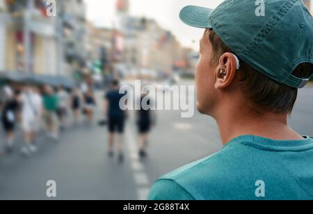 La vie humaine avec une prothèse auditive. Dans une ville bruyante, un jeune homme avec une prothèse auditive à l'oreille entend bien les gens Banque D'Images