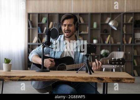 Joyeux jeune homme inspiré jouant de la guitare, enregistrant sa propre chanson. Banque D'Images