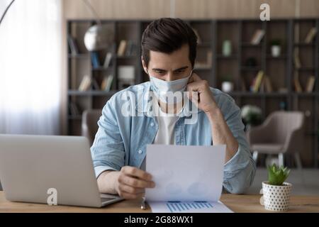 Employé masculin concentré dans un masque facial travaillant pendant la pandémie de covid19. Banque D'Images