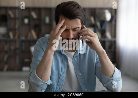 Jeune homme stressé tenant une conversation de téléphone portable dans le bureau. Banque D'Images