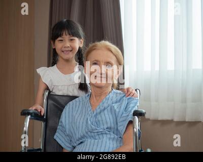 Une petite fille embrasse sa grand-mère assise dans un fauteuil roulant à l'hôpital Banque D'Images