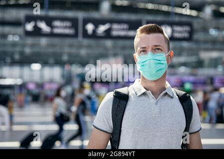 Homme portant un visage protecteur pendant le voyage en avion. Les passagers se trouvent à pied au comptoir d'enregistrement du terminal de l'aéroport. Banque D'Images