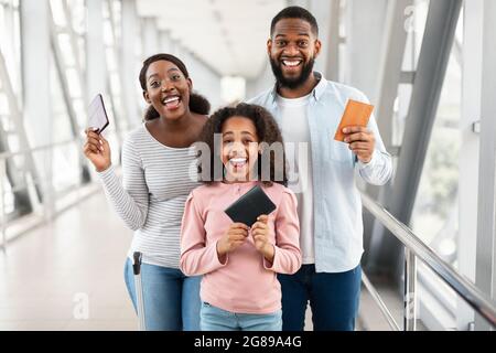 Bonne famille noire excitée voyageant, tenant des documents à l'aéroport Banque D'Images