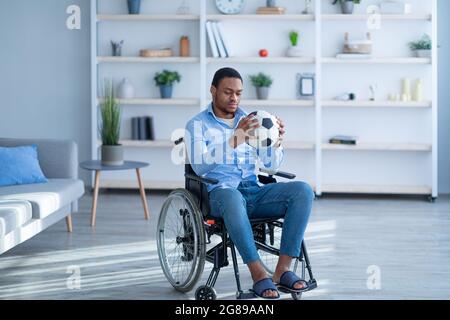 Homme noir handicapé déprimé en fauteuil roulant regardant le ballon de soccer avec tristesse, stressé au sujet de blessures ou de handicap Banque D'Images