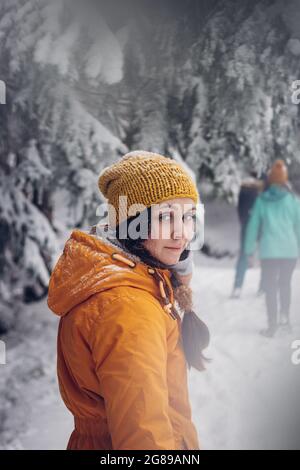 une jeune brune habillée d'une veste orange se présente avec un sourire réaliste et agréable à son petit ami et l'attend. Détendez-vous en hiver. Une promenade dans le natu sauvage Banque D'Images