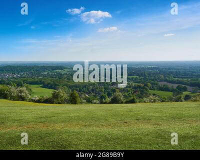 Un large ciel bleu nuageux, une colline verte herbeuse et les villes, les champs et les bois au large d'une vallée du Surrey. Banque D'Images