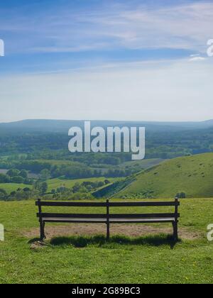 Une vue panoramique sur une vallée et des collines verdoyantes et des bois sous un ciel bleu parsemé de nuages sombres. Un banc invite à s'asseoir et à se reposer. Banque D'Images