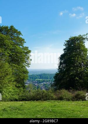 Vue sur le sommet d'une colline entourée d'arbres, sur une vallée verdoyante et bucolique de la campagne et des bois, sous un ciel bleu vif et estival. Banque D'Images