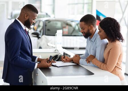 Acheter une nouvelle voiture. Documents de signature des couples afro-américains dans le centre des concessionnaires Banque D'Images