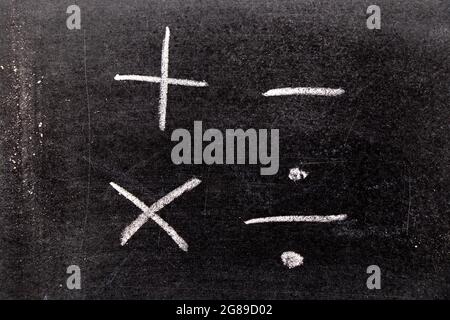 Dessin à la main de la craie blanche en forme de symbole mathématique (plus, moins, multiplier, diviser) sur fond de tableau noir Banque D'Images