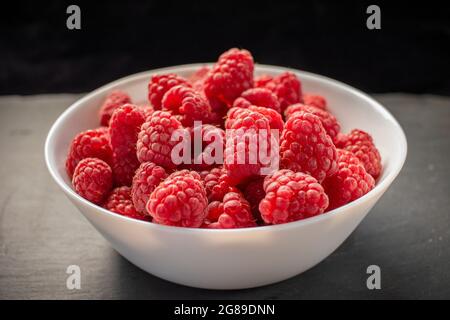 Framboises dans un bol blanc sur fond de pierre noire Banque D'Images