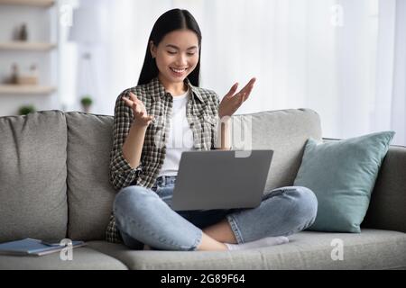 Jolie jeune femme asiatique assise sur un canapé avec un ordinateur portable Banque D'Images