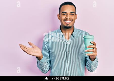 Un jeune afro-américain boit une tasse de café à emporter pour célébrer ses réalisations avec un sourire heureux et une expression gagnante avec une main levée Banque D'Images