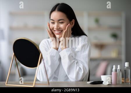 Jolie femme asiatique en peignoir faisant un massage de soulèvement de visage Banque D'Images