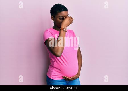 Jeune afro-américaine s'attendant à un bébé, touchant le ventre enceinte fatiguée se frottant le nez et les yeux sensation de fatigue et de maux de tête. Stress et frustrations Banque D'Images