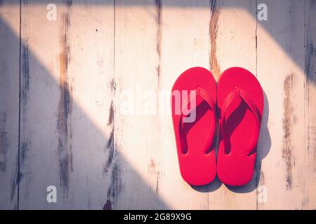 Une paire de pantoufles en caoutchouc rouge coloré populaire utilisation sur une plage de sable et des destinations touristiques tropicales sur fond de bois avec lumière du soleil et espace de copie. Banque D'Images