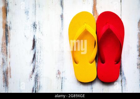 Une paire de pantoufles en caoutchouc rouge et jaune colorées, populaire sur une plage de sable et des destinations touristiques tropicales sur fond de bois avec lumière du soleil et c Banque D'Images