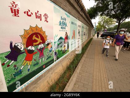 Pékin, Chine. 18 juillet 2021. Les Chinois marchent devant une fresque du Parti communiste vantant les avantages offerts aux enfants par le Parti à Beijing, le dimanche 18 juillet 2021. Les affiches et slogans de style soviétique en Chine ont lancé une campagne de propagande pour promouvoir la nouvelle politique des trois enfants du pays. Photo de Stephen Shaver/UPI crédit: UPI/Alay Live News Banque D'Images