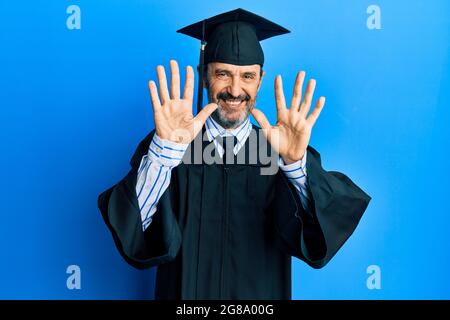 Homme hispanique d'âge moyen portant une casquette de remise des diplômes et une robe de cérémonie montrant et pointant vers le haut avec les doigts numéro dix tout en souriant confiant et heureux. Banque D'Images
