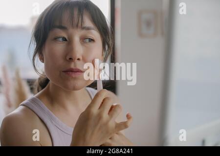 Portrait de femme asiatique utilisant des cosmétiques pierre quartz rouleau pour le massage du visage. Concept de soins de la peau Banque D'Images