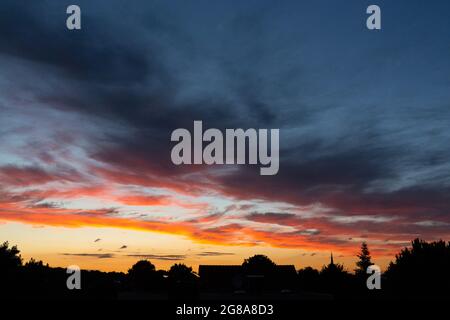 Le coucher du soleil fait briller le ciel en orange, jaune, rouge, bleu, noir, blanc sur la silhouette d'un paysage. Banque D'Images