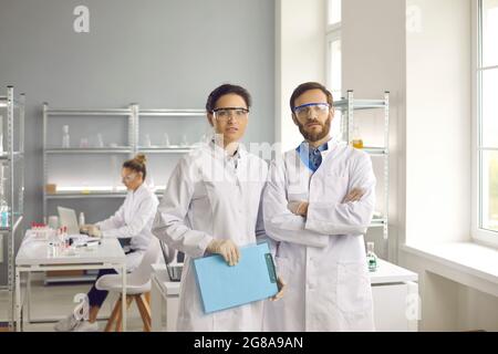 Portrait de scientifiques en blouses de laboratoire et lunettes de protection debout dans un laboratoire médical moderne Banque D'Images