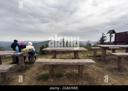 WIELKI Lubon, Pologne - 15 juillet 2021: Groupe de personnes assises sur un banc en bois à un sommet de montagne polonaise pendant le temps pluvieux nuageux situé dans un Banque D'Images