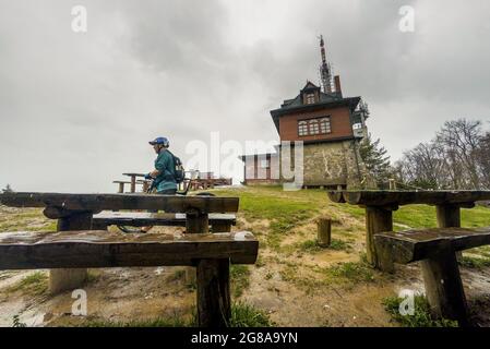 WIELKI Lubon, Pologne - 15 juillet 2021 : un homme avec un VTT ou un vélo derrière un banc en bois au sommet d'une montagne polonaise par temps pluvieux nuageux Banque D'Images