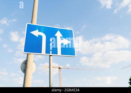 Panneau de signalisation bleu indiquant les règles de virage sur les voies de circulation avec un ciel bleu sur l'arrière-plan. Banque D'Images