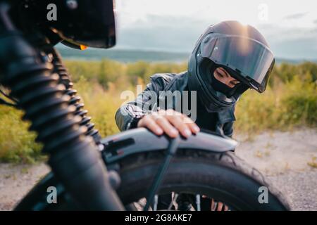 Portrait d'une automobiliste confiante dans un casque assis près de la moto. Jeune conducteur cycliste à l'extérieur au coucher du soleil. Banque D'Images