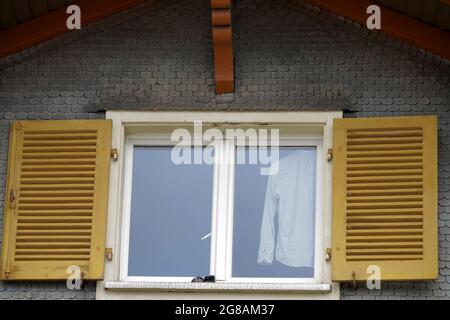 Chemise blanche suspendue dans la fenêtre. Les fenêtres ont des volets jaunes qui sont ouverts. Banque D'Images