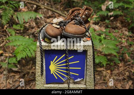 Camino de Santiago (chemin de Saint James). Chaussures de pèlerin placées sur le kilomètre traditionnel de la Camino de Santiago près de la ville d'Arzúa en Galice, Espagne. La route française et la route nord du Camino de Saint-Jacques traversent cette ville peu avant que les deux routes atteignent Saint-Jacques-de-Compostelle. La coquille de pétoncle, également connue sous le nom de la coquille de Saint-Jacques, est représentée dans le jalon comme un symbole traditionnel du pèlerinage à Saint-Jacques-de-Compostelle. Banque D'Images