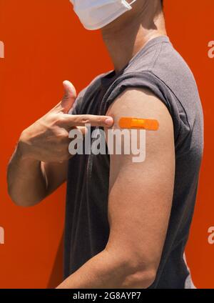 Vaccins, pansement sur le concept de bras de personnes vaccinées. Orange bande de couleur sur le bras de l'homme fort qui pointe son propre épaule après vaccinati Banque D'Images