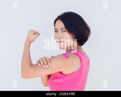 Vaccins, bandage sur les personnes vaccinées concept. Femme asiatique confiante en réservoir rose montrant le plâtre de bandage montrant un geste fort avec le poing ha Banque D'Images