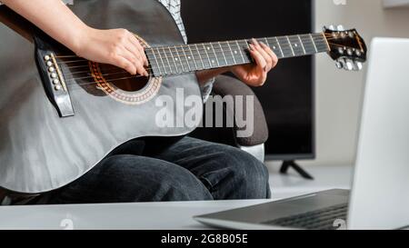 Guitare musicale en ligne. Une jeune femme joue de la guitare acoustique à la maison pour le public en ligne sur ordinateur portable. Cours de cours en ligne de guitare Banque D'Images