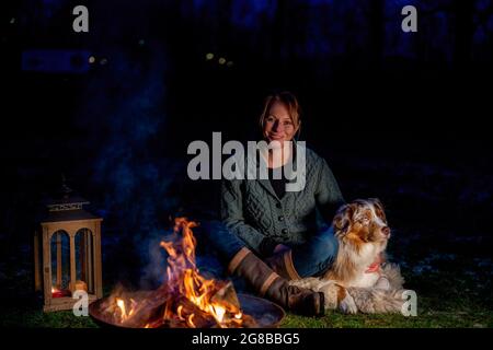 Le chien est assis près du feu de camp avec son propriétaire. La femme regarde avec amour le Berger allemand. Vacances en hiver, feu de bougie dans lanterne Banque D'Images