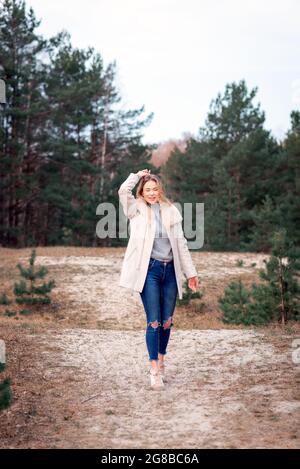 Jeune belle blonde longue cheveux femme debout vue de face avec les mains levées sur fond vert naturel extérieur. Jeune femme bras élevés appréciant Banque D'Images