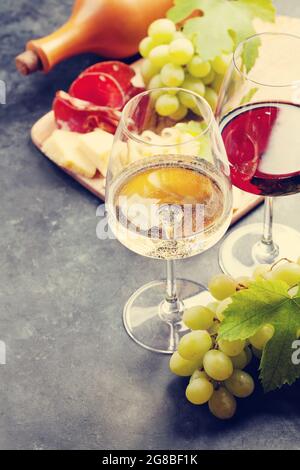 Verres à vin blanc et rouge, planche à raisins et hors-d'œuvre avec fromage et prosciutto Banque D'Images