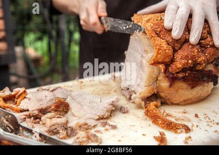 Gros plan sur la main du chef en coupant une viande de porc rôtie typiquement italienne dans le jardin du restaurant pour un déjeuner ou un brunch Banque D'Images