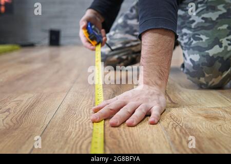 concept de réparation, de bâtiment et de maison - gros plan des mains mâles mesurant le plancher en bois. pose de sol stratifié. Mesure de la surface de l'appartement Banque D'Images