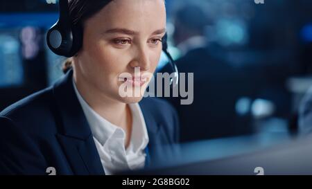 Gros plan Portrait d'un très beau spécialiste de l'assistance technique à la clientèle qui parle d'un micro-casque tout en travaillant sur un ordinateur dans une surveillance sombre Banque D'Images