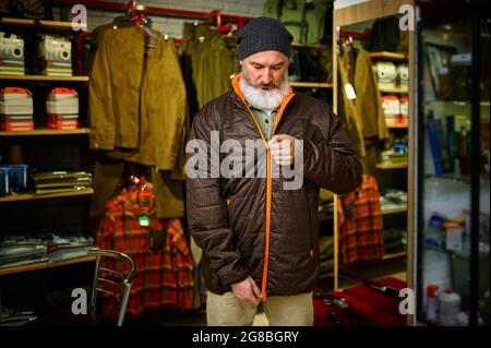 Le chasseur barbu tente sur la veste en duvet dans le magasin d'armes à feu Banque D'Images