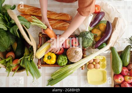 Les mains de la jeune femme prenant du pain frais, des fruits et des légumes qu'elle a achetés au supermarché sur une table de cuisine Banque D'Images