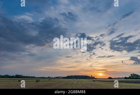 Des rouleaux de foin au champ au lever du soleil avec des nuages incroyablement beaux. Banque D'Images