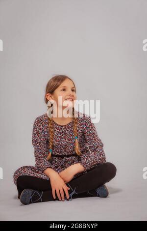 Petite fille riante assise à pattes croisées sur le sol, isolée sur blanc. Banque D'Images