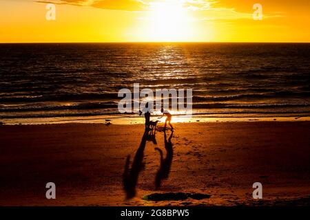 Un chien accueille ses propriétaires après avoir nagé dans la mer d'Irlande à Helen's Bay, Co. Down, au lever du soleil sur le solstice d'été. Banque D'Images