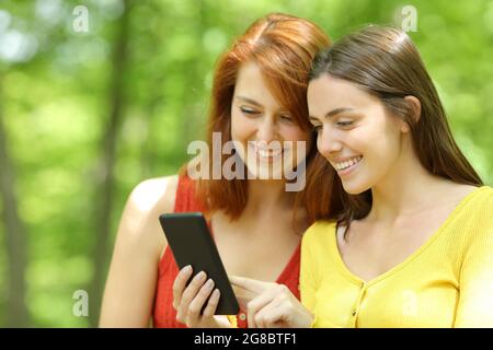 Deux amis heureux vérifiant un smartphone dans un parc vert Banque D'Images