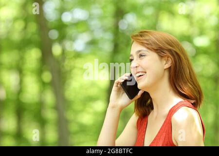 Une femme heureuse qui appelle sur un téléphone mobile à pied dans un parc vert Banque D'Images