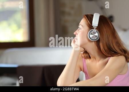 Une femme sérieuse se détend en écoutant de la musique avec un casque sans fil regardant par une fenêtre dans la chambre Banque D'Images