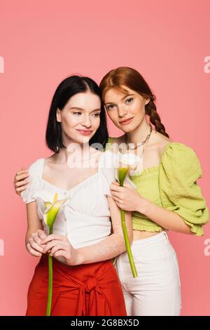 Freckled femme tenant calla Lily près de l'élégant ami avec le vitiligo isolé sur le rose Banque D'Images